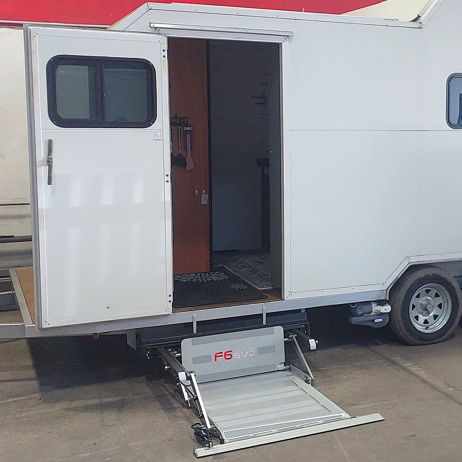 A caravan with an underbody hoist installed at the door.