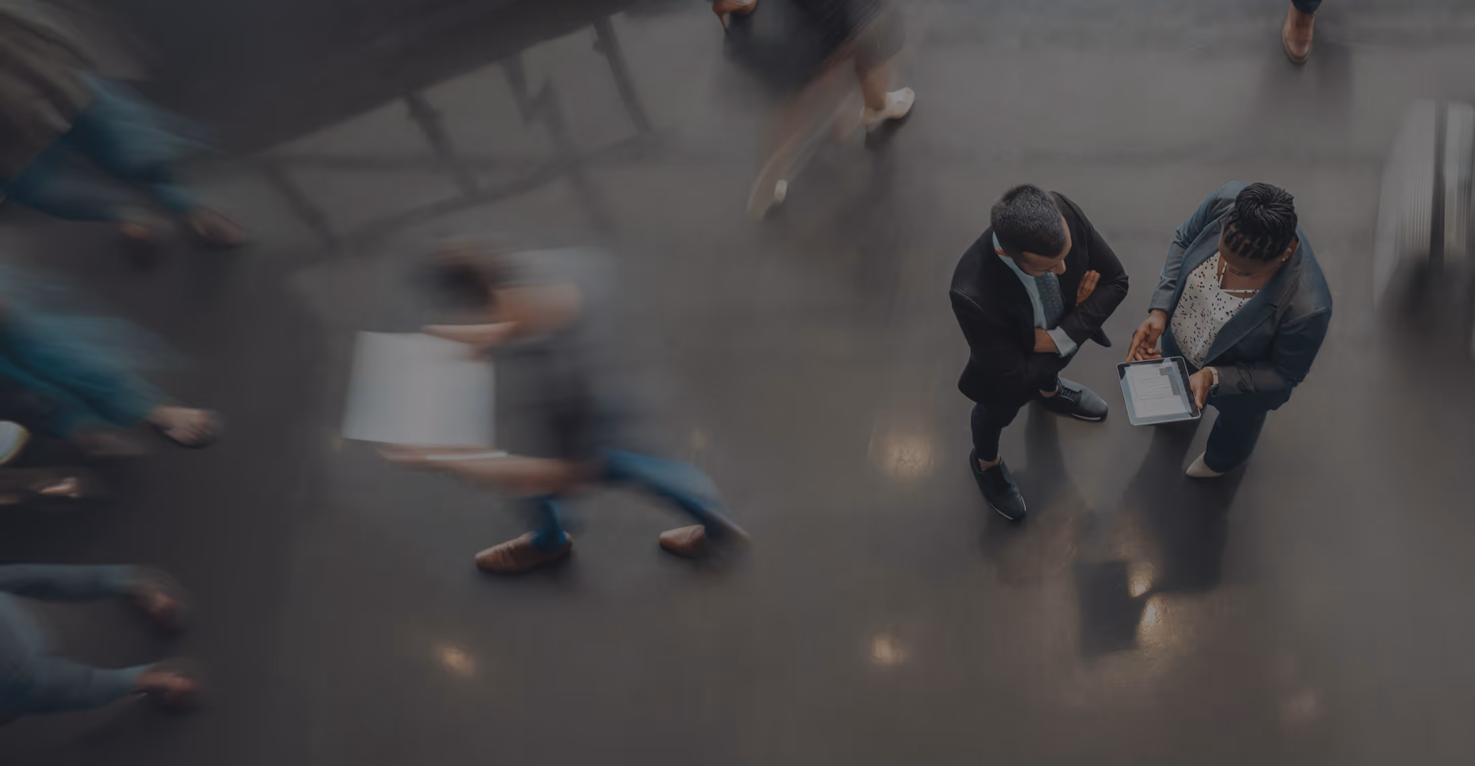 Overhead view of people walking on a shiny floor with two individuals standing and reviewing a tablet.