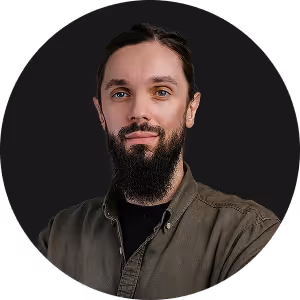 Man with dark hair and beard, wearing a green button-up shirt, posing against black background.