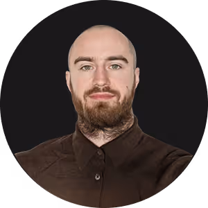 Portrait of a bald man with a beard and neck tattoo wearing a dark shirt against a black background.