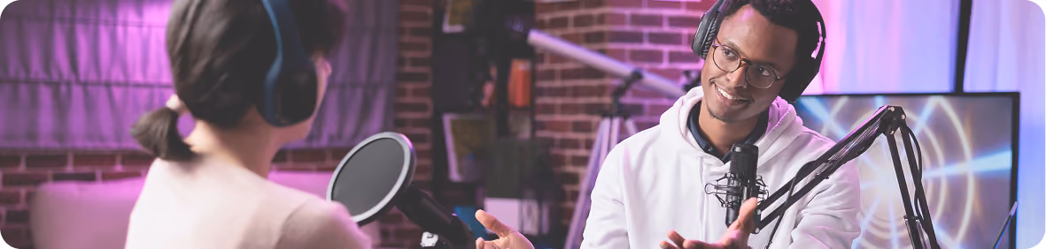 Two people recording a podcast in a studio with microphones and headphones, purple lighting.