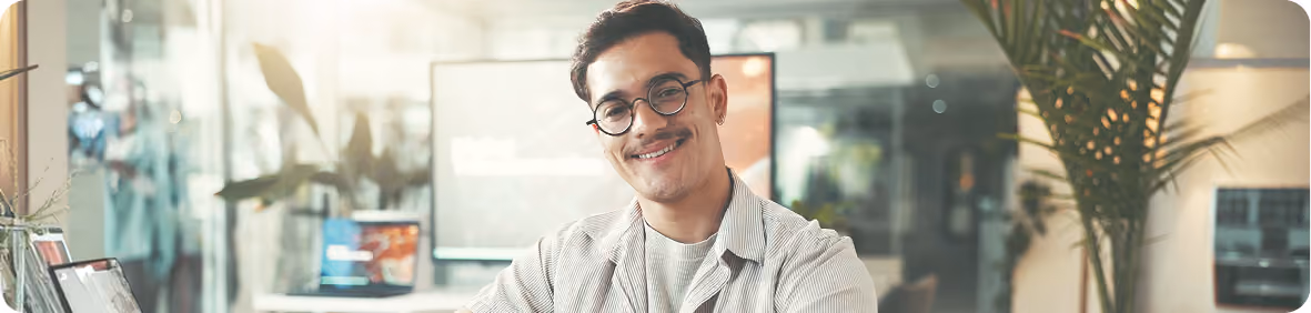 Smiling man with round glasses and striped shirt in a bright modern office environment.