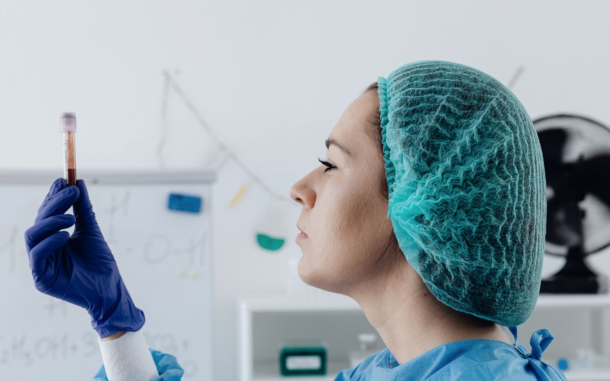 Pharmaceutical specialist in a hairnet checking a sample vial