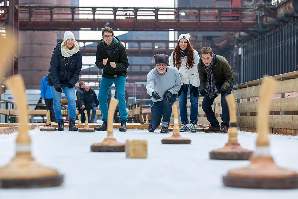 Gruppe von Leuten beim Eisstockschiessen vor Industriekulisse auf dem Welterbe Zollverein