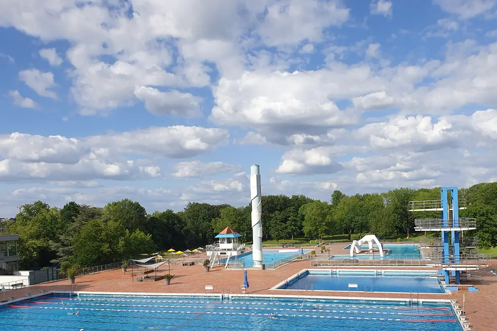 Blick auf das Grugabad mit wettkampffähigen Schwimmbecken mit einem 10-Meter-Turm vor blauem Himmel, Essen