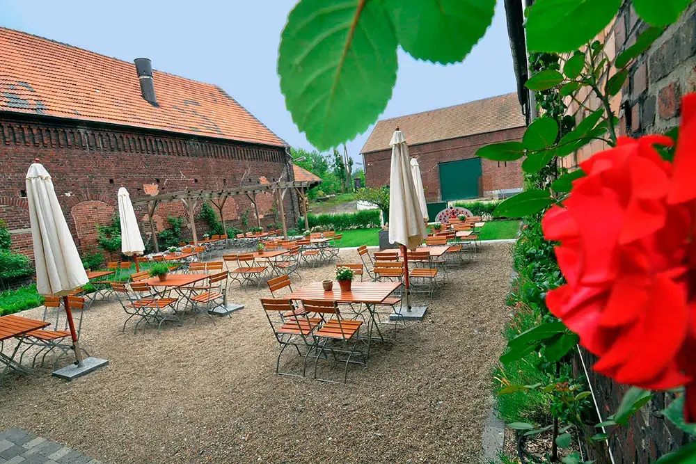Gemütliches Bauernhof-Cafe mit Klappstühlen vor Holztischen neben Sonnenschirmen umgeben von historischem Gehöf, Hofmarkt Bauernhof am Mechtenberg, Essen, Rührgebiet
