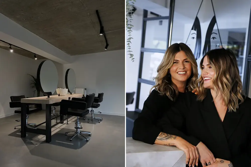 Blick in minimalistisch eingerichteten Friseursalon. Zwei junge Frauen mit blonden Haaren und einem Lächeln im Gesicht hinter Empfangstheke aus Naturstein. Minopoli Hair & Make-Up Artists