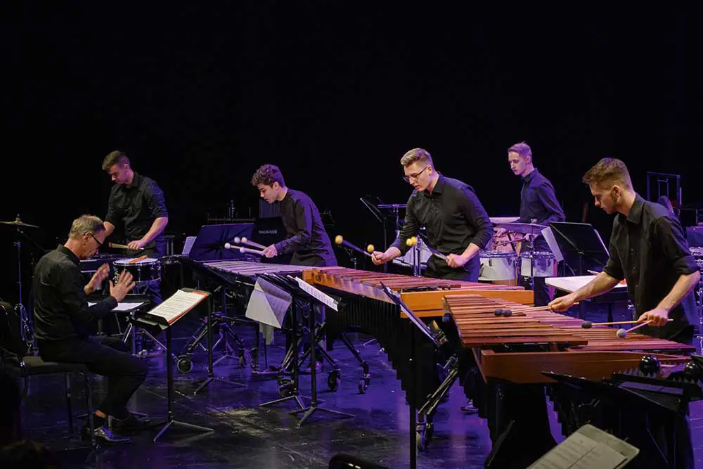 Percussionisten stehen auf einer Konzertbühne und spielen rhythmische Instrumente