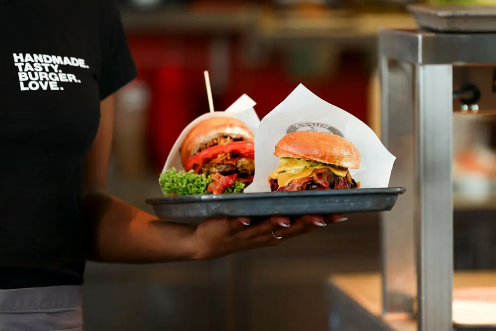 Junge Frau hält Tablett mit Burger-Varianten im Restaurant. © Ruff‘s Burger