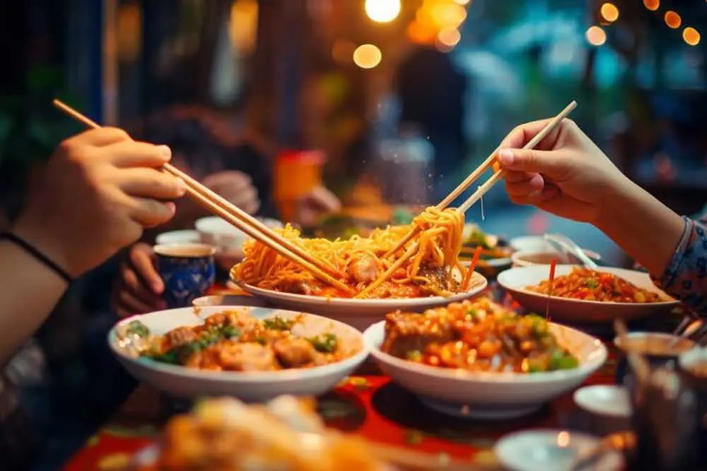 Nahaufnahme von jungen Menschen, die chinesisches Essen am Tisch mit Stäbchen essen