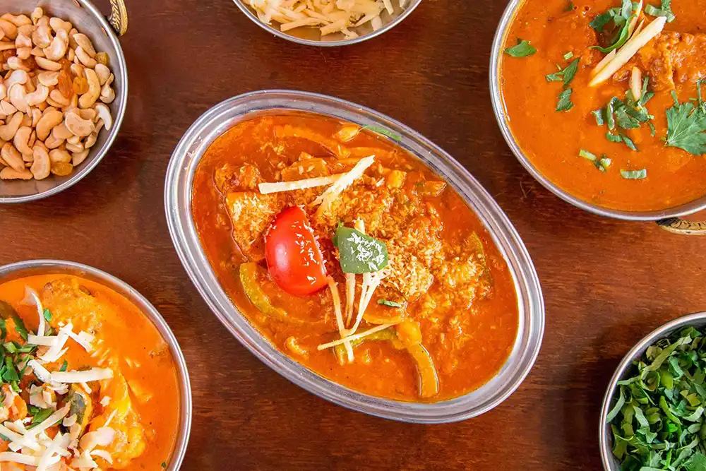 Indische Currys wie Butter Chicken und Tikka Masala in Silberschalen auf rotem Hintergrund