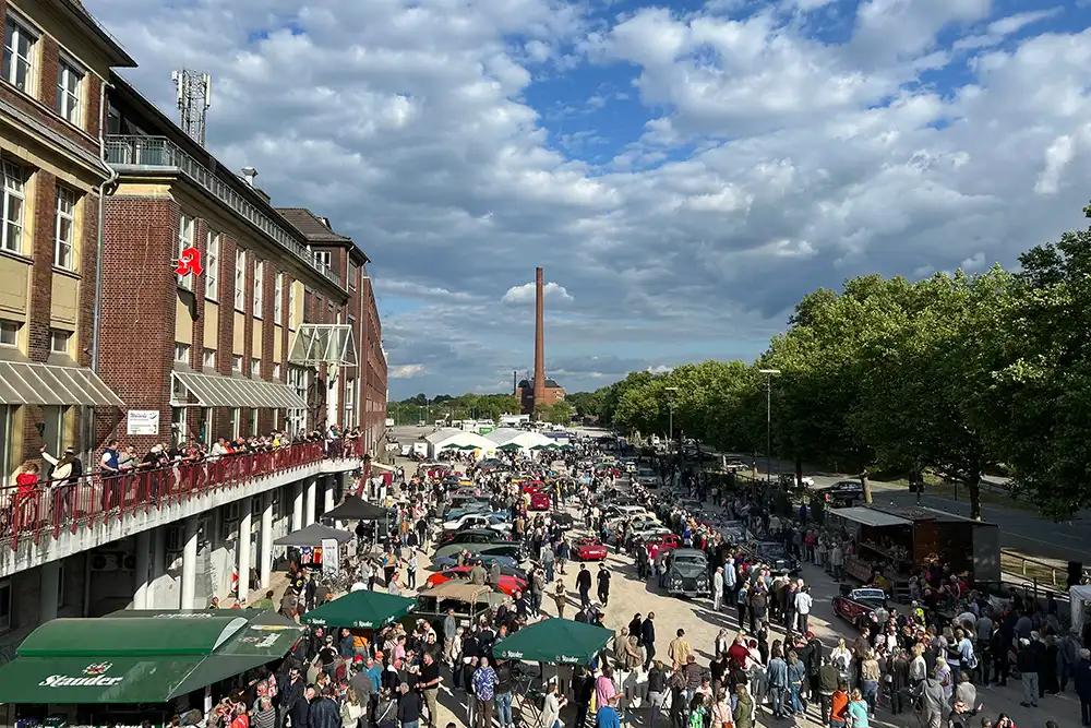 Vogelperspektive eines Oldtimertreffens bei sonnigem Wetter mit grünen Marktschirmen, Food-Ständen und Besuchern
