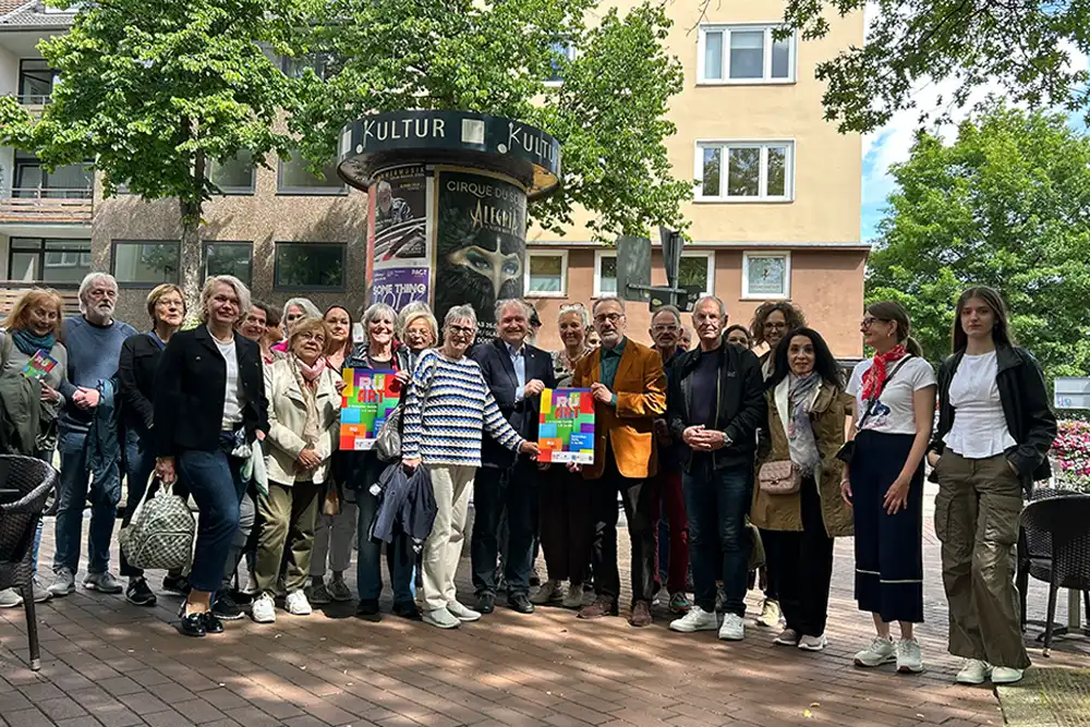 IMG_1838rueart-kunstmeile-ruettenscheid-offguide Rü Art Rüttenscheider Kunstmeile 2026 Essen: Eine Gruppe von Menschen präsentiert die bunten Veranstaltungsplakate vor einer Kulturlitfaßsäule.
