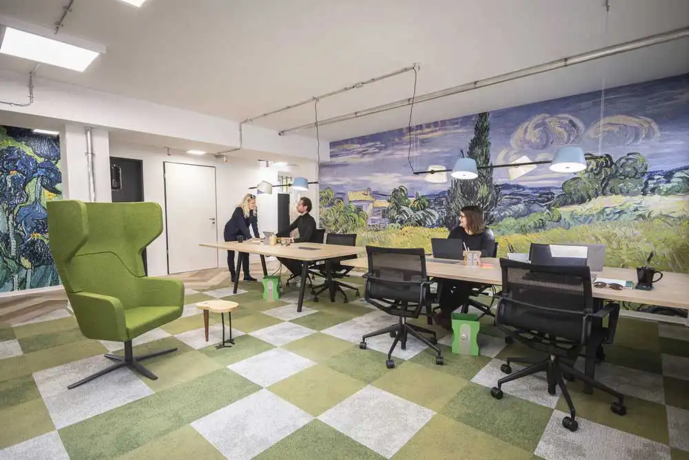 Kreativer Besprechungsraum im Coworking Space mit Van-Gogh-Wandbild, grünem Teppich und modernen Arbeitsplätzen