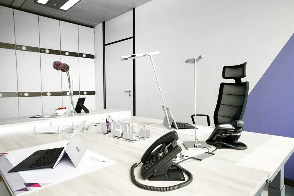 Modernes Chefbüro mit hellem Schreibtisch, ergonomischem Bürostuhl, Telefonen und Laptops im minimalistischen Design