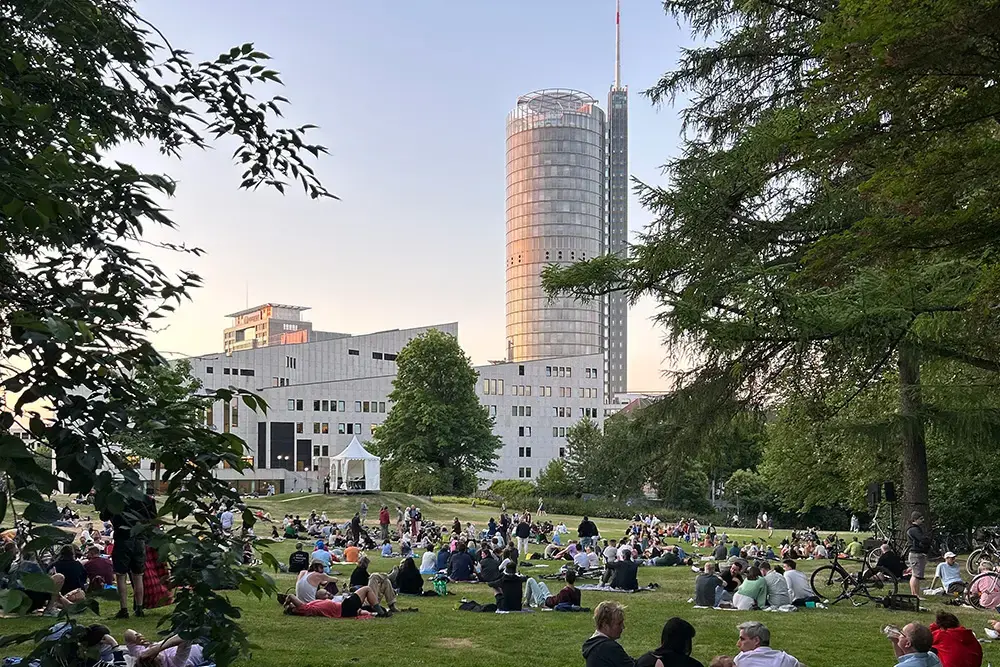 Viele Menschen picknicken auf der großen Wiese im Stadtgarten Essen im Südviertel mit Blick auf das Aalto-Theater und den RWE-Turm.