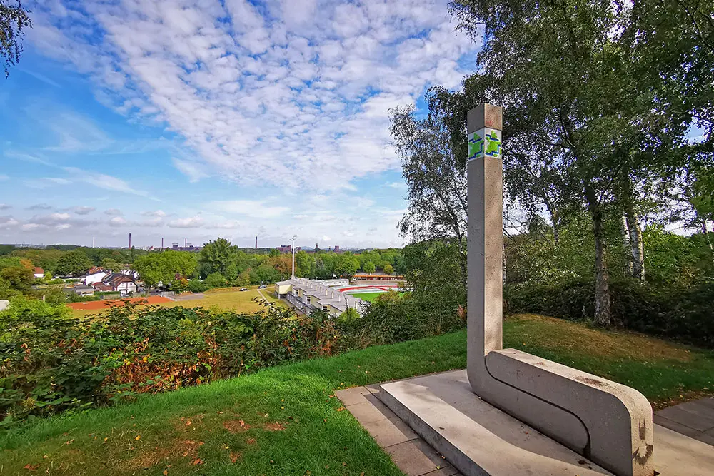 Aussichtspunkt im Hallopark in Essen-Stoppenberg mit einer Betonsäule und Panoramablick auf die Zeche Zollverein im Hintergrund.
