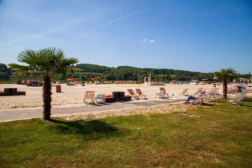Der Sandstrand des Seaside Beach am Baldeneysee in Essen mit Palmen und Liegestühlen an einem sonnigen Sommertag.