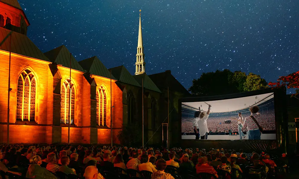 Zuschauer:innen beim Lichtburg Open Air Kino am beleuchteten Essener Dom unter einem sternenklaren Sommerhimmel.