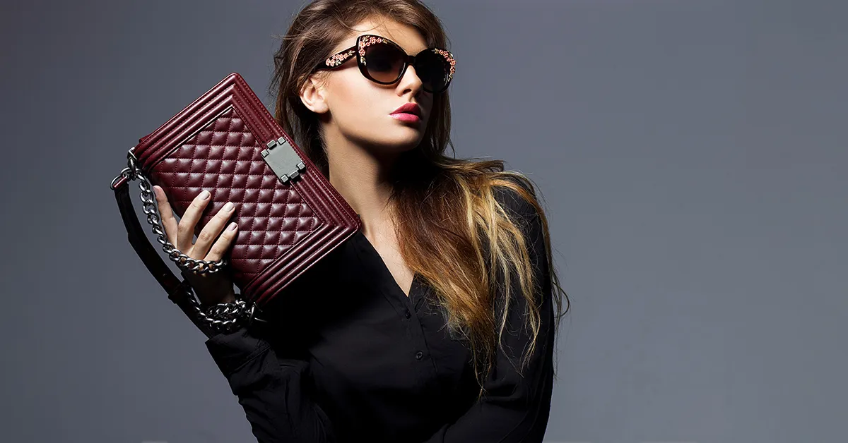Modèle en lunettes de soleil design posant avec un sac à main pour dames.