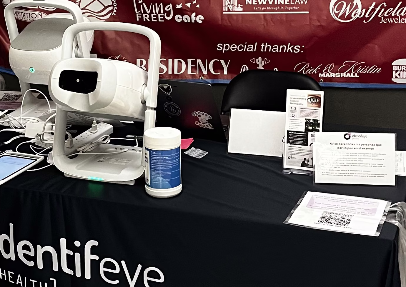 identifeye retinal camera on a clinic table with patient information sheets, in front of a RAM event sponsor banner
