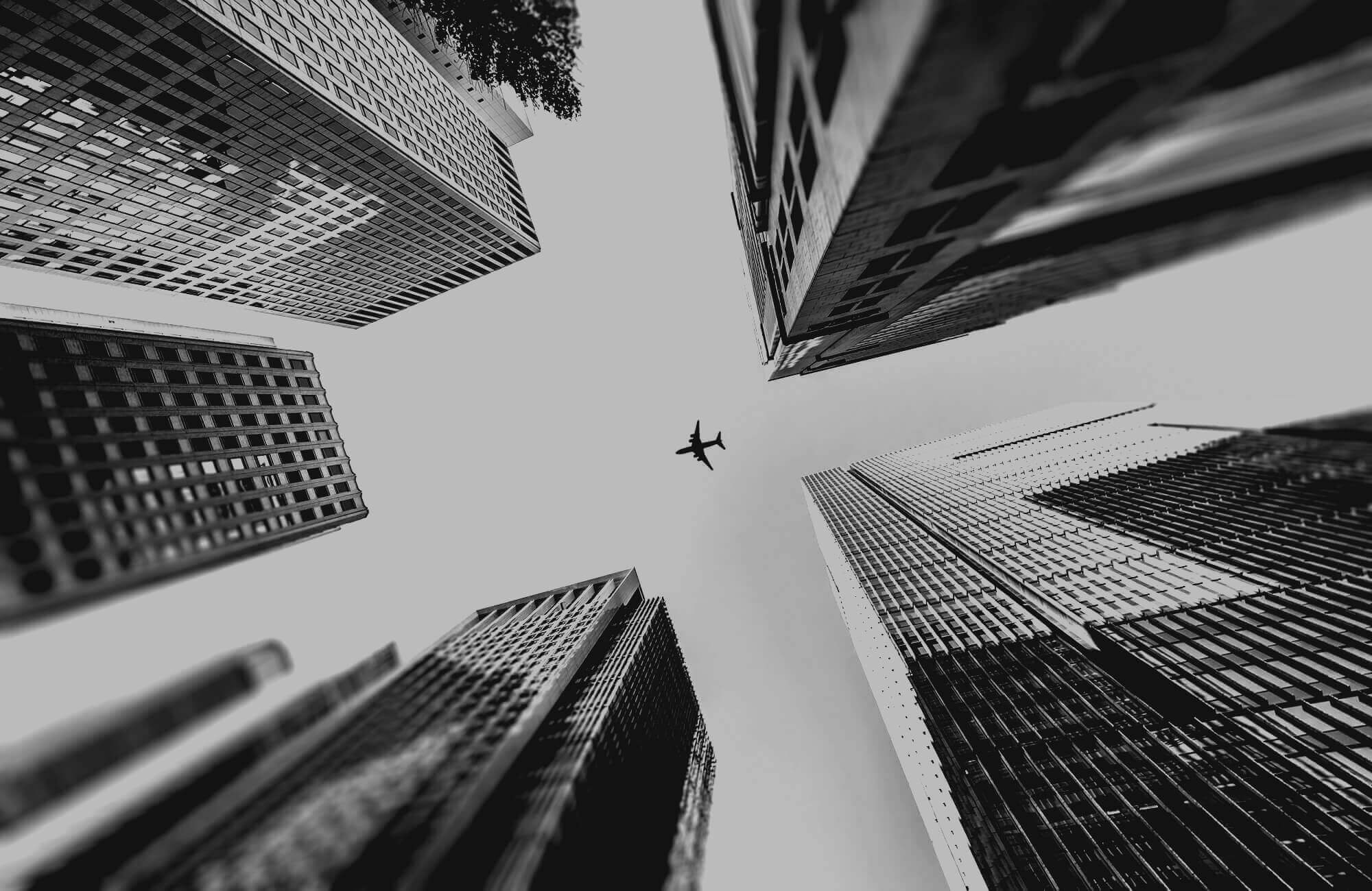 Photo looking up at skyscrapers with an airplane flying overhead in the center.