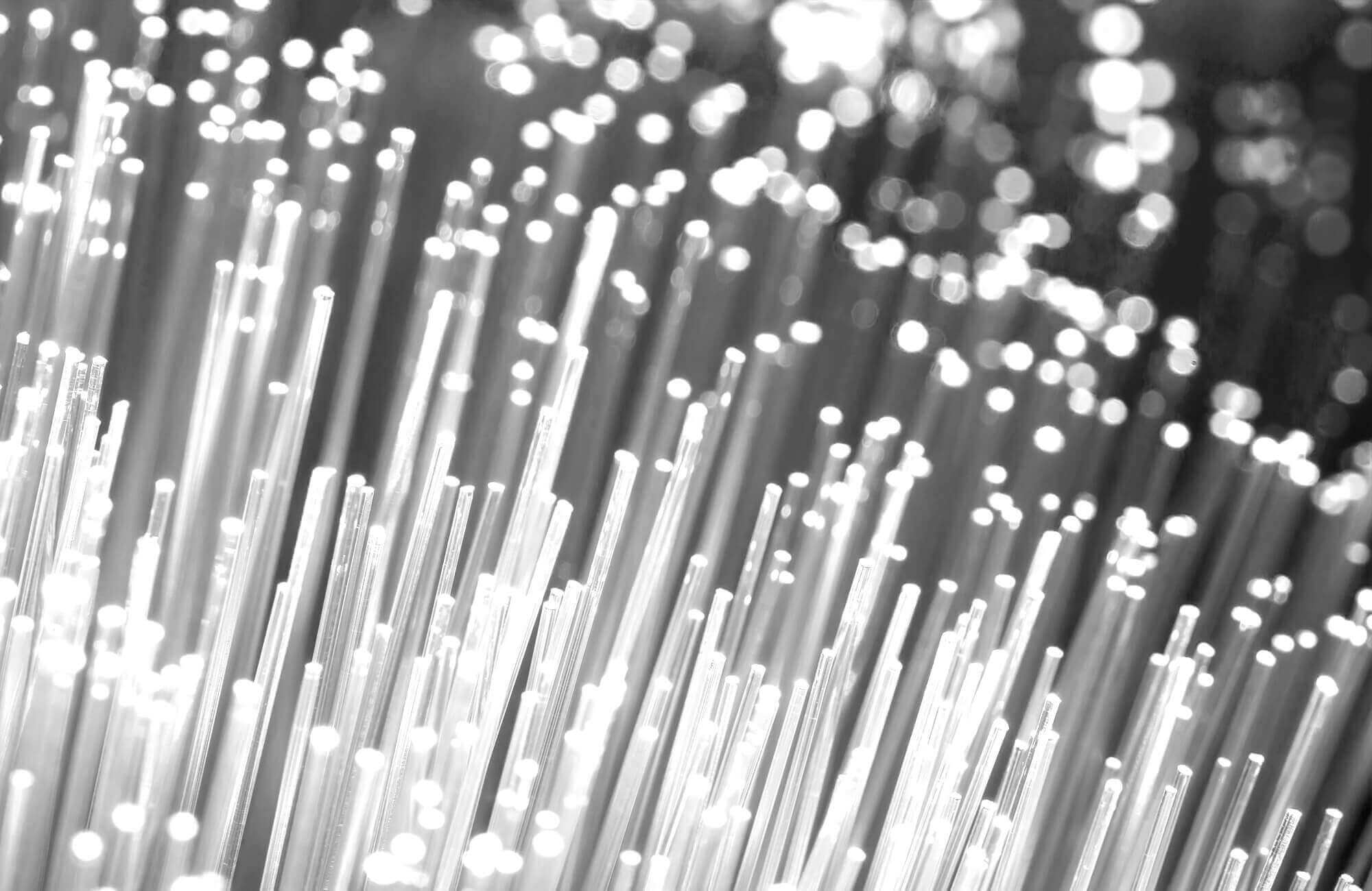 Close-up of glowing fiber optic cables emitting bright white light in a dark background.