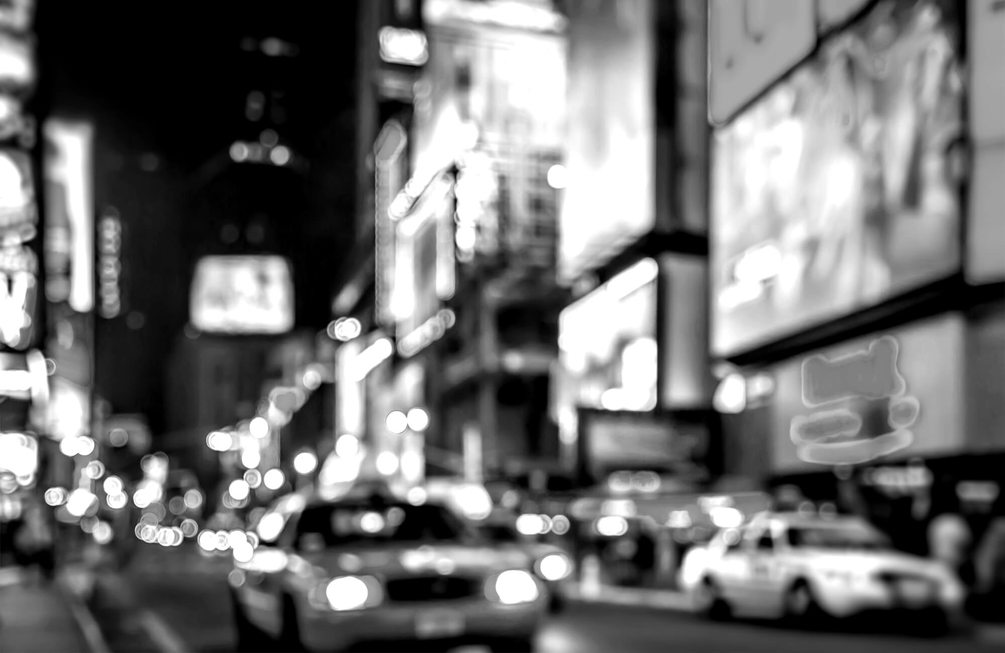 Blurred city street scene at night with cars and bright billboard lights.