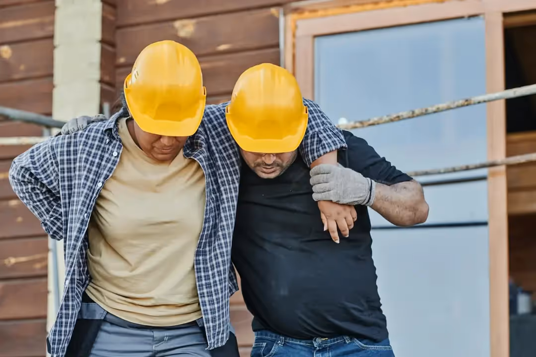 A photo of an injured construction worker being assisted by his colleague.