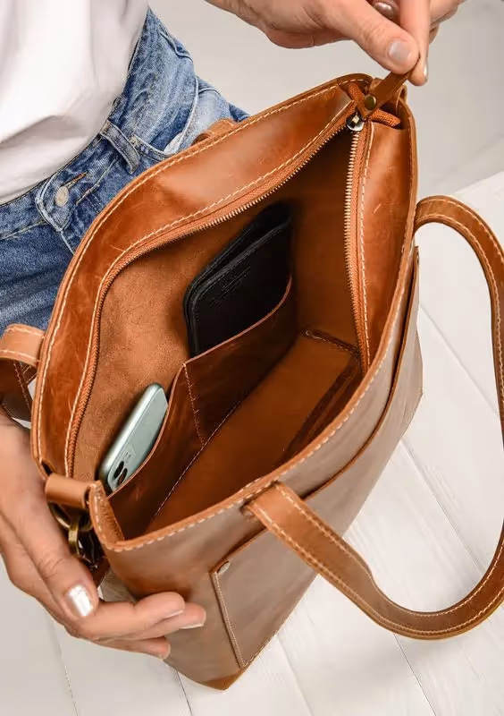 Business Casual Dress Code for Client-Side Project Managers: a photo of a person opening the handbag. Inside the bag is a mobile phone and a wallet.