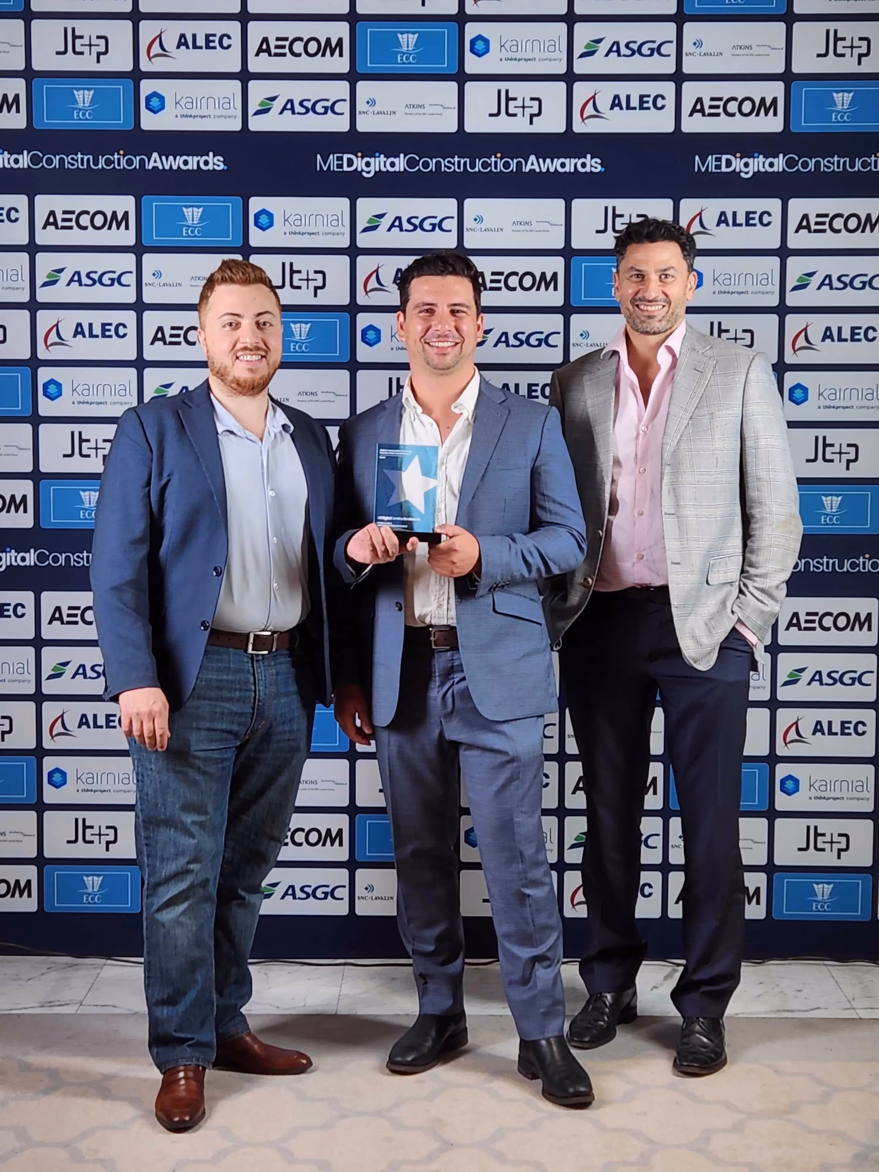 Three project managers pose with an award they receive in front of a media wall