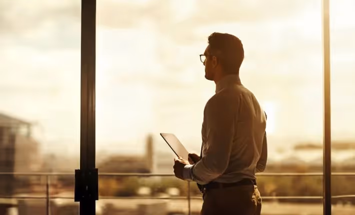 Project Manager vs Program Managers: Differences and Interdependencies: a male professional looking over at a window.