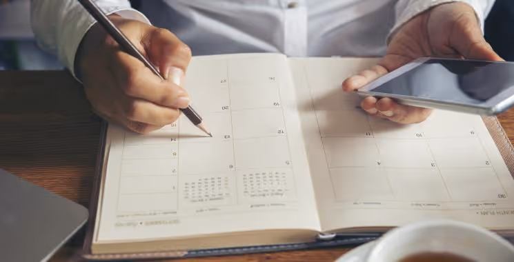 Person planning Rostered Days Off (RDO) in Australia using a calendar and phone.