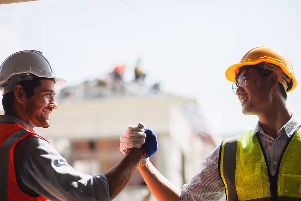 Two construction workers shake hands, symbolizing teamwork and program controls in project coordination.