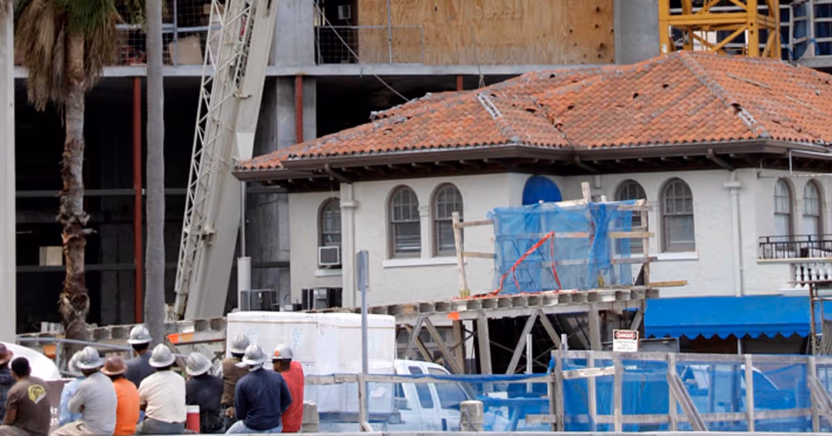 Workers watch as a crane section is lifted from the roof of a Miami house after falling from a high-rise under construction, causing fatal damage.