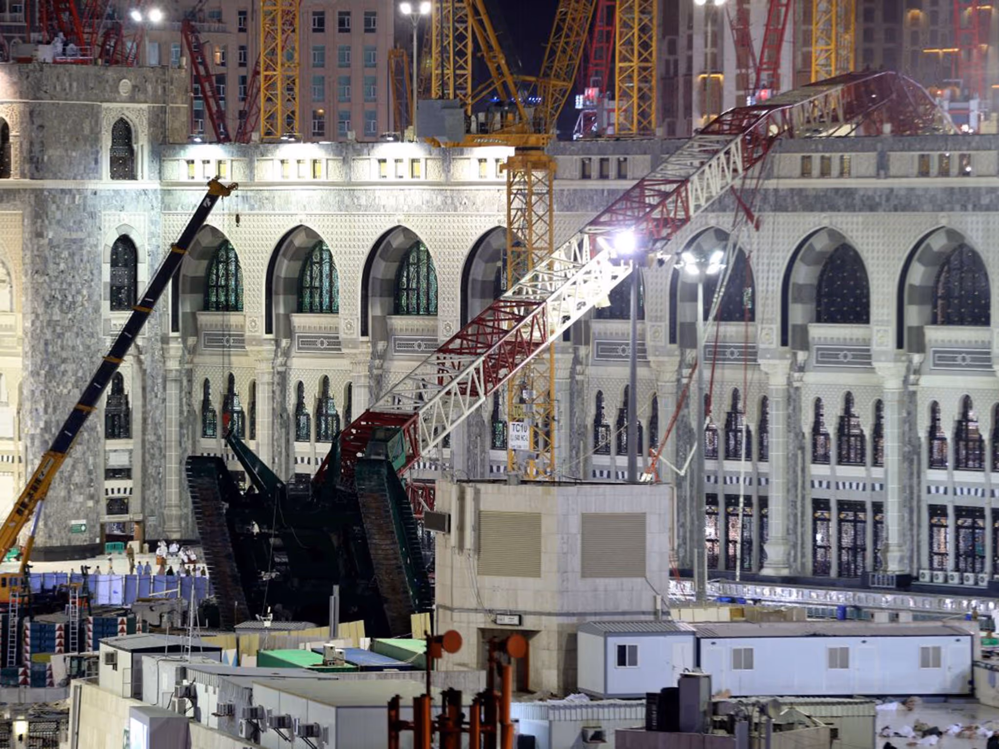 Large red-and-white crane toppled over the Grand Mosque courtyard in Mecca, surrounded by other cranes and construction equipment at night.