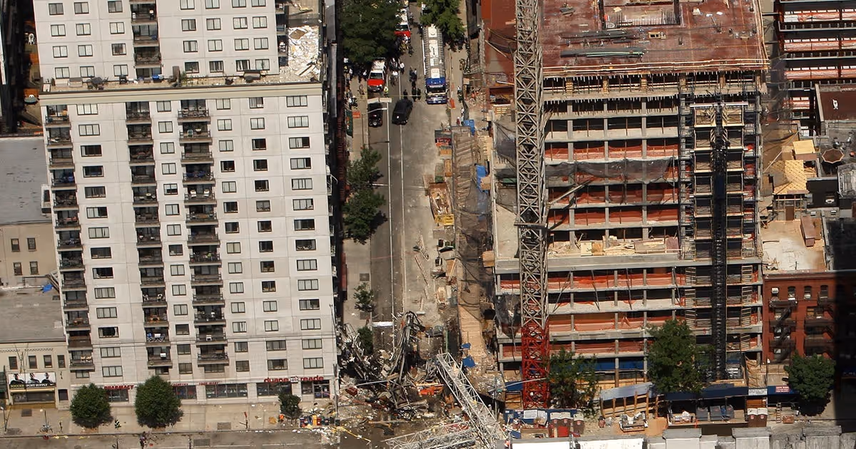 Aerial view of a collapsed crane lying across a narrow street in Manhattan, with debris between a high-rise apartment building and a construction site.