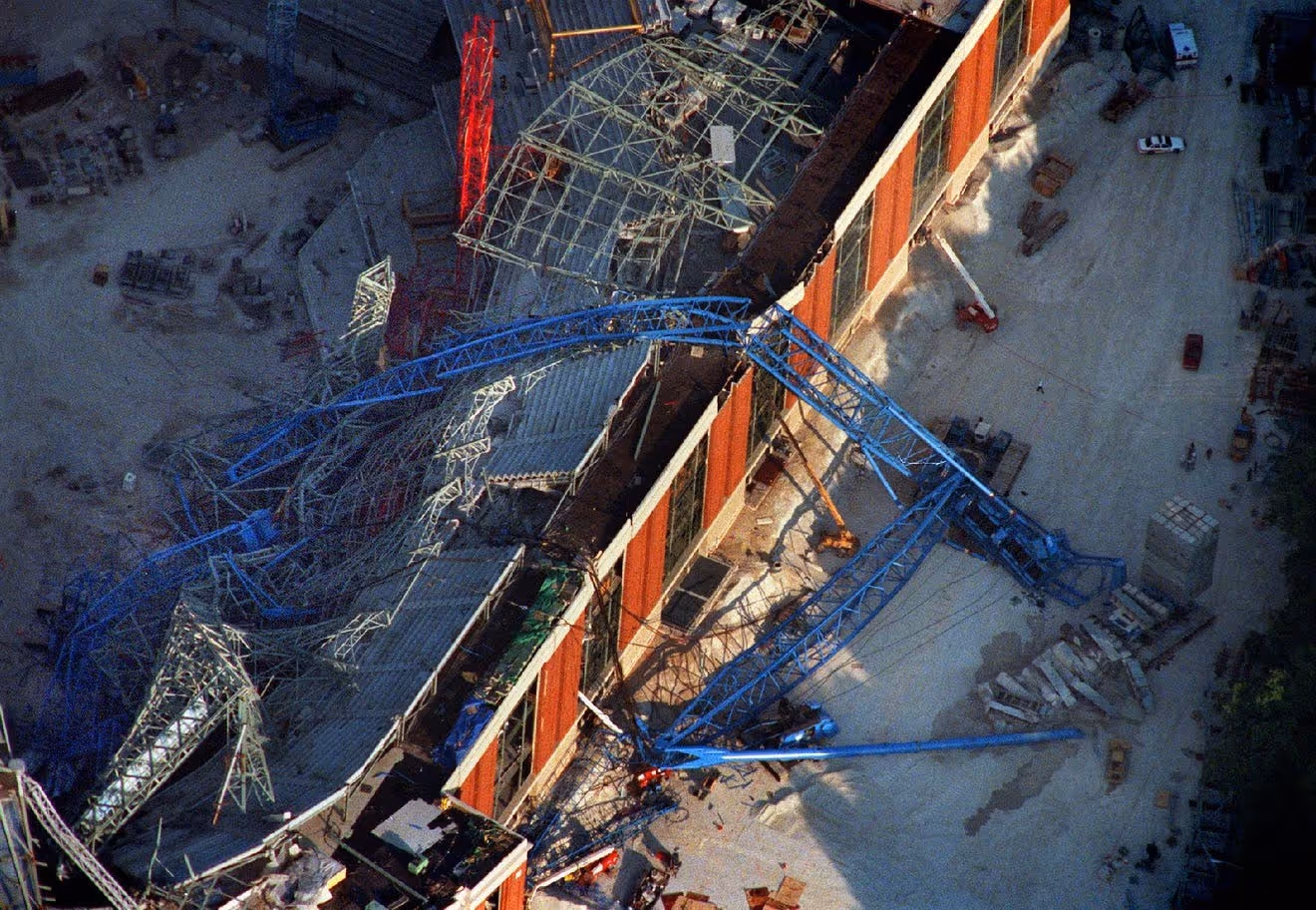 Aerial view of collapsed blue crane across Miller Park construction site, with twisted steel trusses and structural damage to the stadium's outer wall.