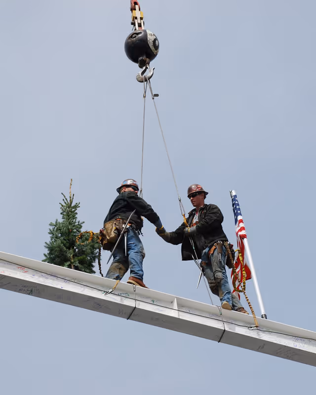 Construction workers shake hands atop beam during topping out ceremony