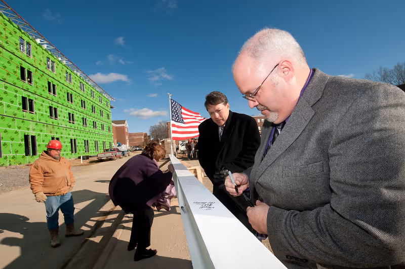 People sign steel beam during topping out ceremony at construction site