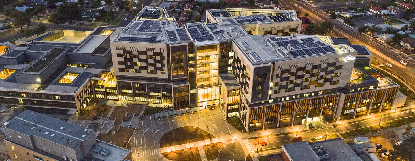 Aerial view of Bendigo Hospital at dusk showing its large, modern complex with solar panels and brightly lit interior spaces.