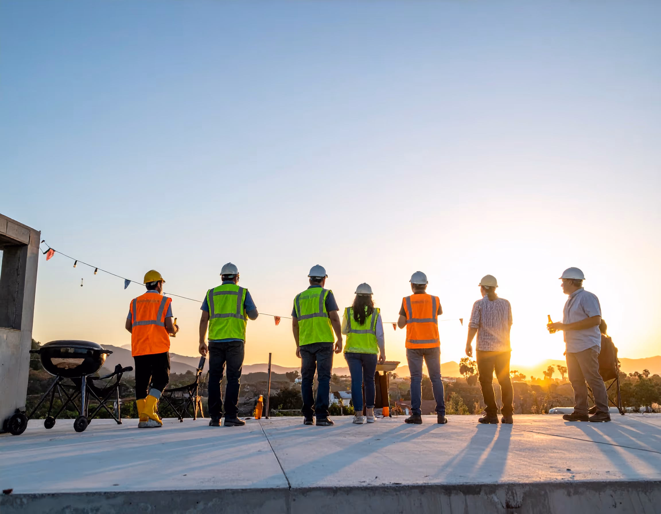  Construction team holding a slab party at sunset with BBQ and drinks on a newly poured concrete slab.