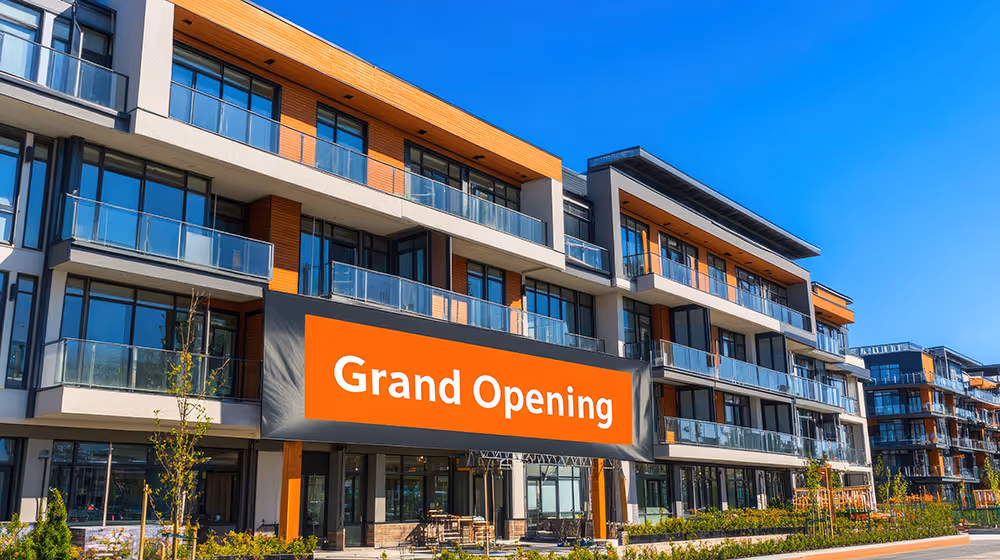 Modern apartment complex with large “Grand Opening” banner displayed outside.