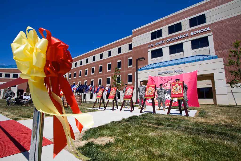 Soldiers stand in front of Hatcher Hall during a building dedication ceremony with a ribbon cutting display.