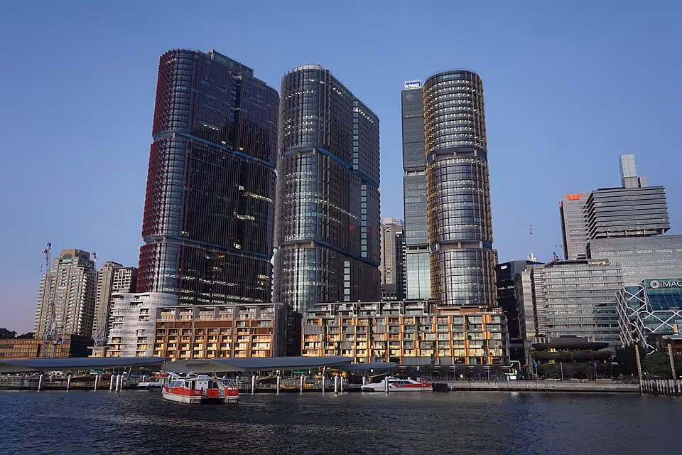 Skyline view of International Towers Barangaroo in Sydney with three modern glass office towers beside the harbor at dusk.
