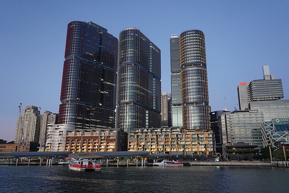 Skyline view of International Towers Barangaroo in Sydney with three modern glass office towers beside the harbor at dusk.