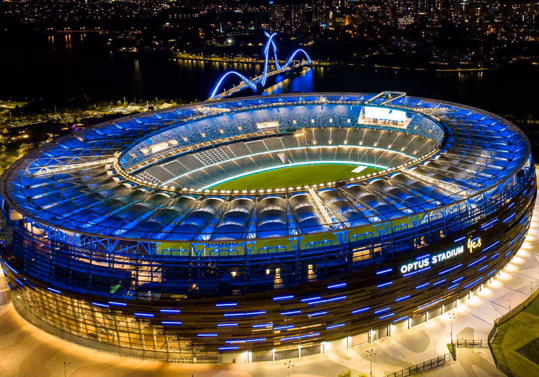 Aerial night view of Optus Stadium in Perth with illuminated roof and seating, showing its circular structure and event-ready setup.