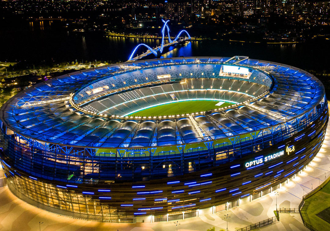 Aerial night view of Optus Stadium in Perth with illuminated roof and seating, showing its circular structure and event-ready setup.