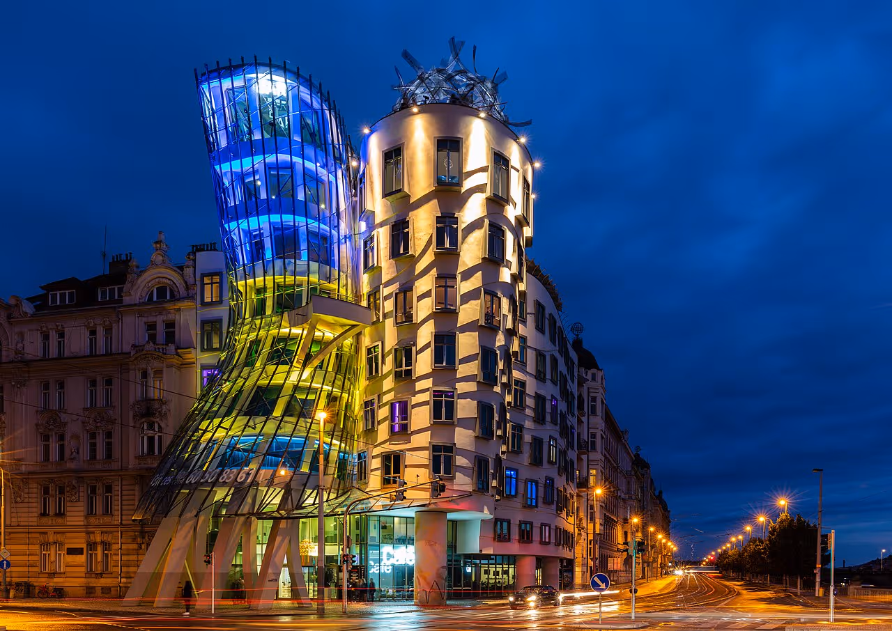 A curving glass and concrete building lit with colorful lights, resembling a pair of dancers in motion.