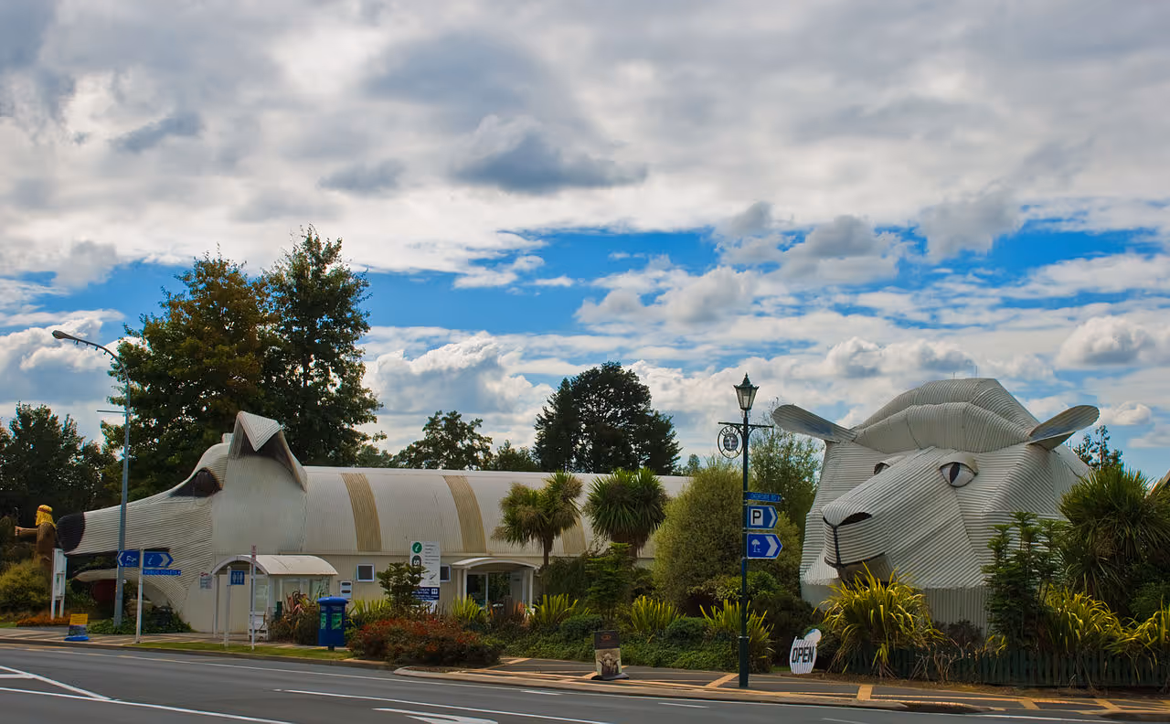 Two novelty buildings shaped like a sheep and a sheepdog, made from corrugated metal, used as visitor centers in New Zealand.